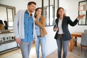 A home inspector examines an attic with a flashlight while a homebuyer observes nearby.