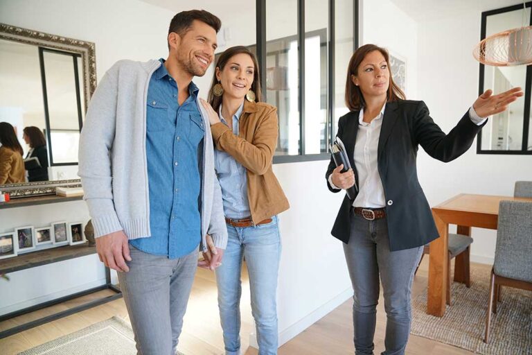 A home inspector examines an attic with a flashlight while a homebuyer observes nearby.