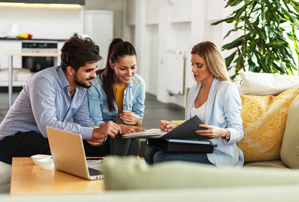 A couple reviews real estate documents with a pen and calculator at a kitchen table.
