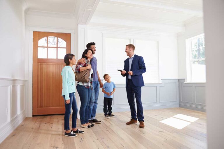 A couple in casual clothes seated at a table with a real estate agent, reviewing property documents together.